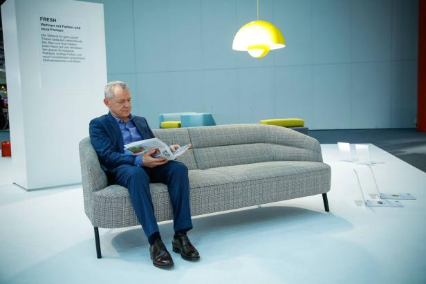 Ein Mann im Anzug sitzt auf einem Sofa und liest eine Zeitschrift.