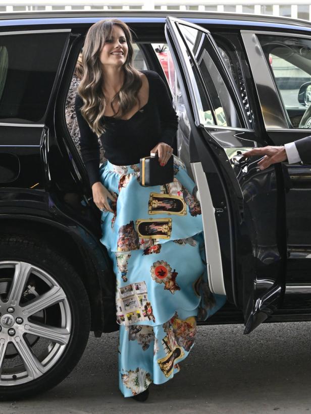 Eine Frau steigt mit einer Handtasche aus einem schwarzen Auto.