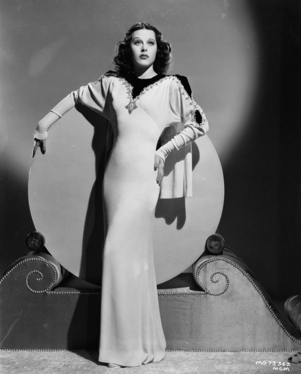 Hedy Lamarr posiert in einem langen, hellen Kleid vor einem runden Hintergrund.