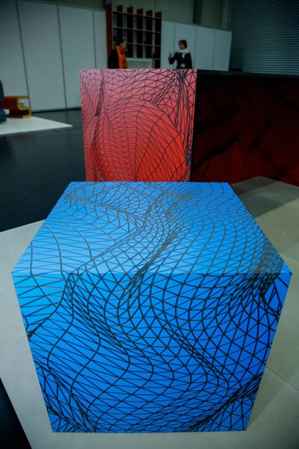 Ein blauer, würfelförmiger Hocker mit einem schwarzen, geometrischen Gittermuster.