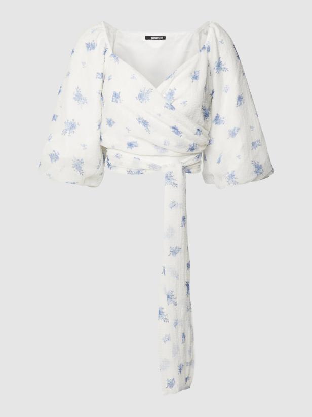 Eine weiße Wickelbluse mit blauem Blumenmuster und Puffärmeln.