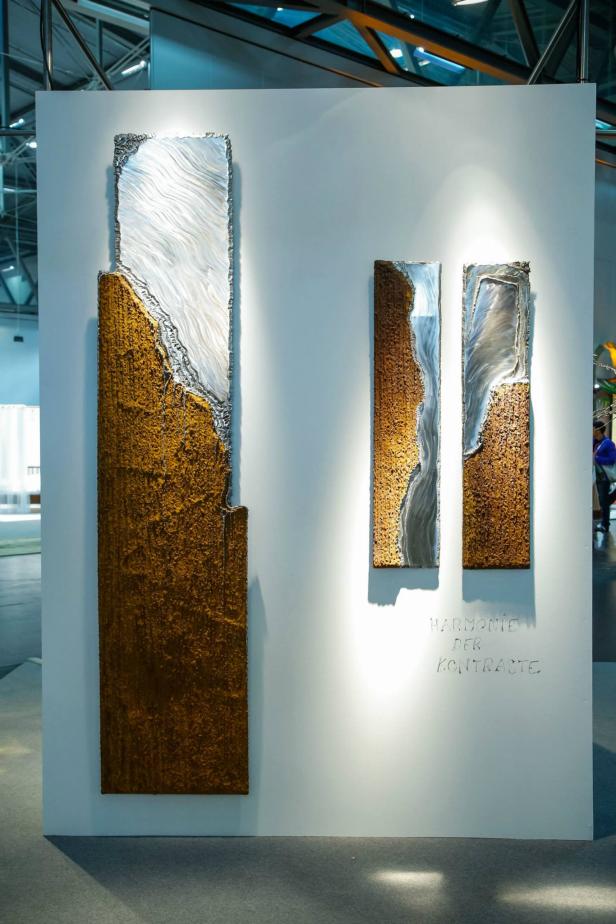 Drei Wandkunstwerke mit abstrakten Formen in Gold und Silber hängen an einer weißen Wand.