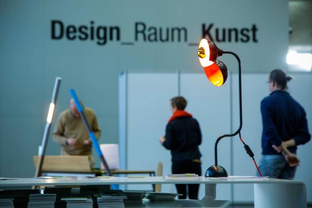 Eine Lampe beleuchtet einen Tisch vor der Aufschrift „Design_Raum_Kunst“.