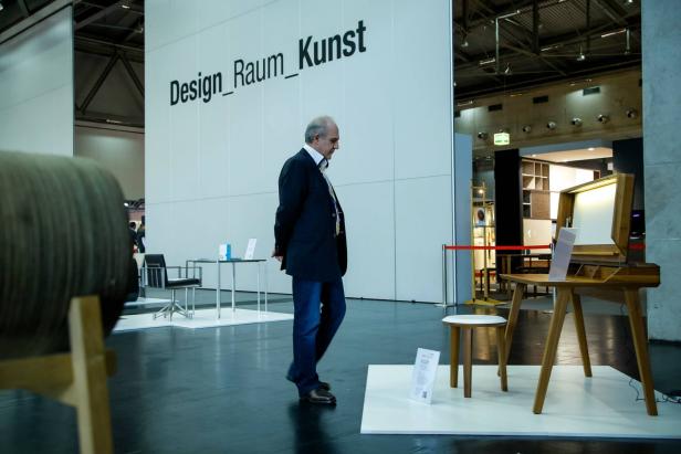 Ein Mann geht an einem Stand mit der Aufschrift „Design_Raum_Kunst“ vorbei.