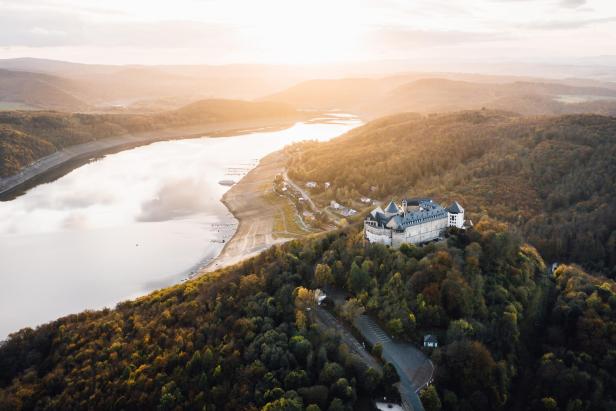 Luftaufnahme der Burg Altena über dem herbstlichen Wald und dem See.