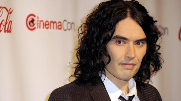 Porträt von Russell Brand mit dunklen, lockigen Haaren vor einem CinemaCon-Hintergrund.