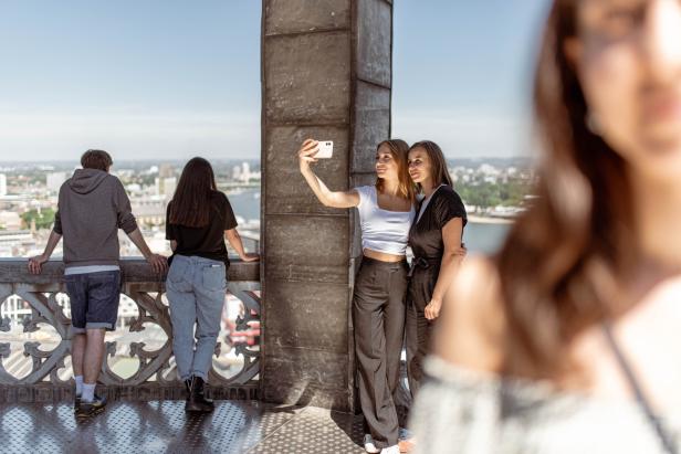 Zwei Frauen machen ein Selfie auf einer Aussichtsplattform mit Blick auf die Stadt.