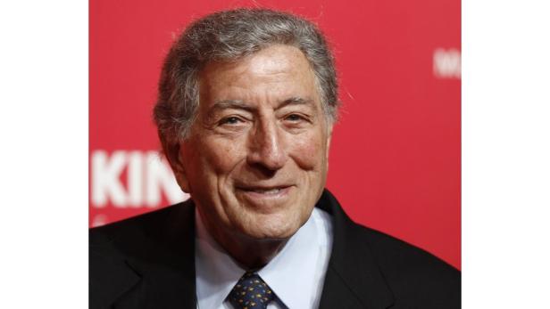 Porträt des lächelnden Sängers Tony Bennett vor einem roten Hintergrund.