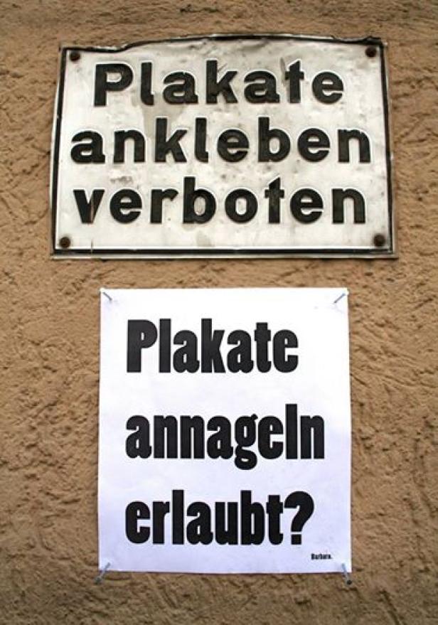 Ein Schild verbietet das Ankleben von Plakaten, während ein anderes das Annageln erlaubt.
