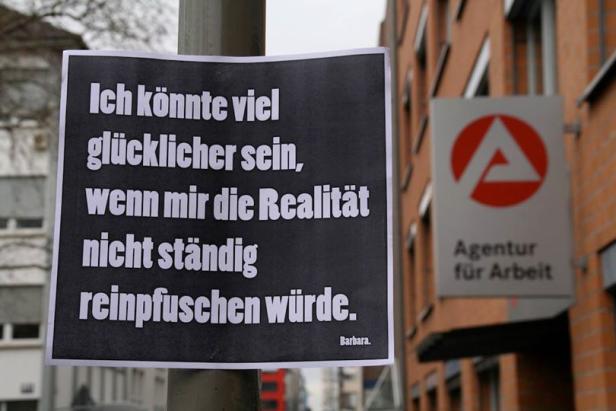 Ein Schild mit dem Zitat: „Ich könnte viel glücklicher sein, wenn mir die Realität nicht ständig reinpfuschen würde.“ hängt vor der Agentur für Arbeit.