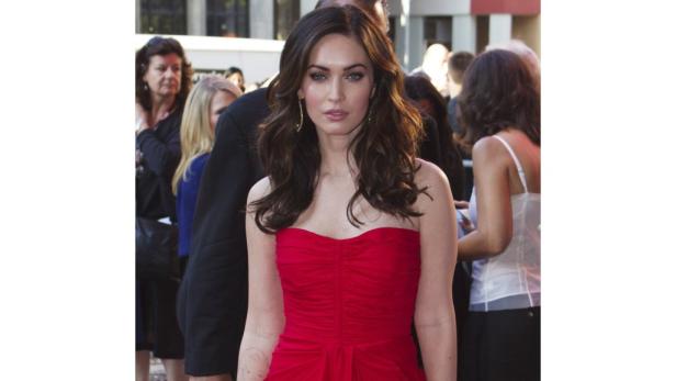 Megan Fox in einem roten, trägerlosen Kleid auf einem roten Teppich.