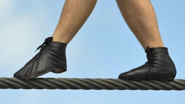 Ein Mann balanciert in schwarzen Schuhen auf einem Drahtseil.