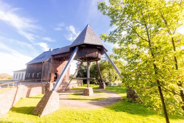 Ein hölzernes Gebäude mit einem markanten Turm auf einer grünen Wiese.
