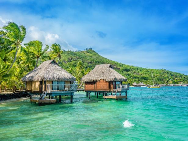 Zwei strohgedeckte Bungalows stehen auf Stelzen im türkisfarbenen Wasser.