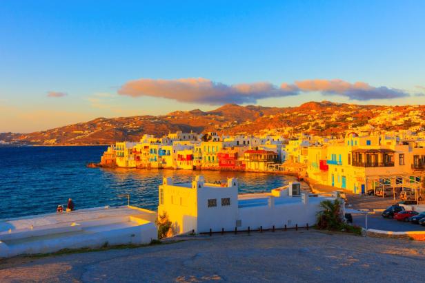 Blick auf Mykonos-Stadt mit farbenfrohen Häusern am Wasser bei Sonnenuntergang.