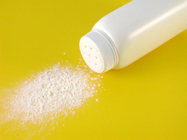 Eine Dose Babypuder liegt auf einer gelben Oberfläche, daneben eine kleine Puderwolke.