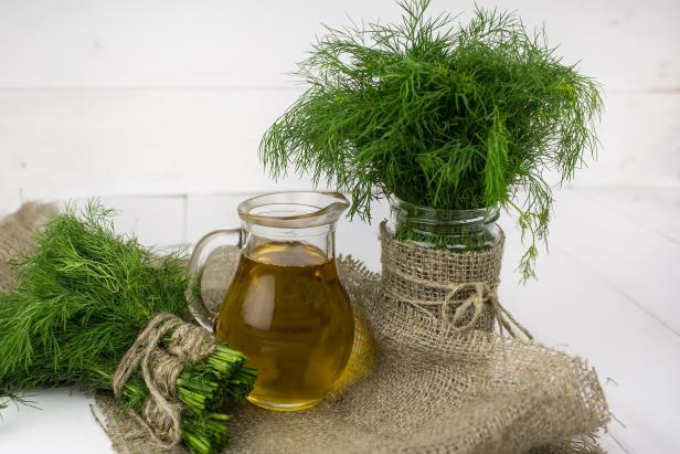 Ein Bund Dill, ein Glas Dill und ein Krug mit Öl auf einem Tisch.