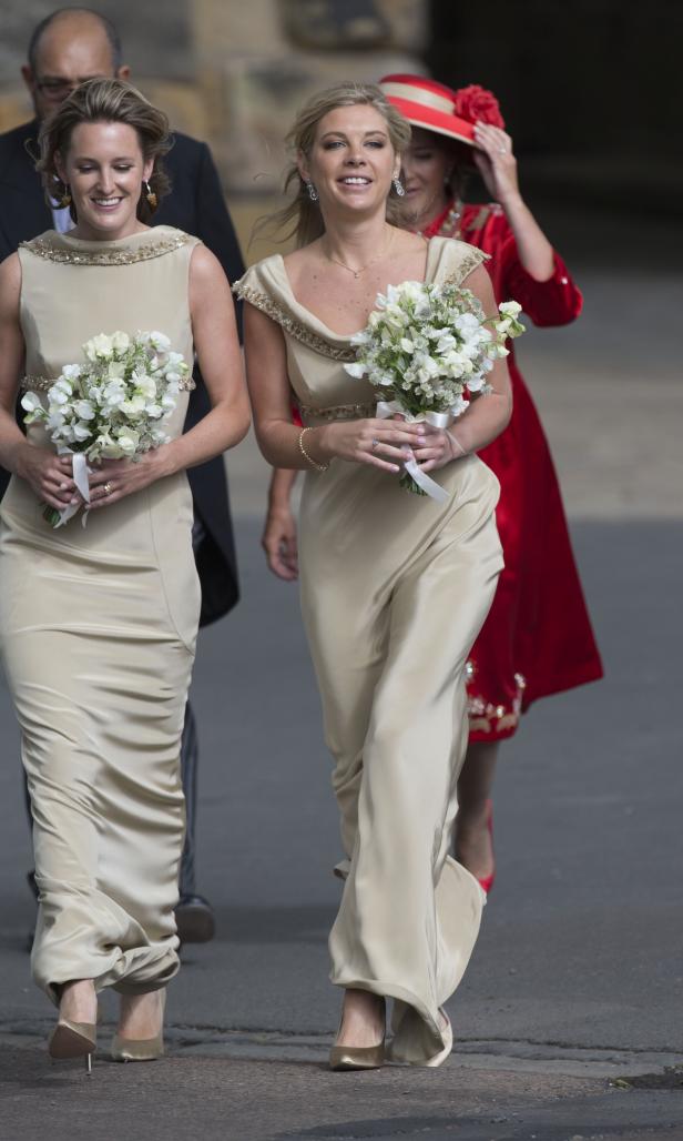 Zwei Frauen in champagnerfarbenen Kleidern mit Blumensträußen gehen auf der Straße.