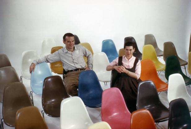 Charles und Ray Eames sitzen inmitten einer Sammlung ihrer farbenfrohen Stühle.