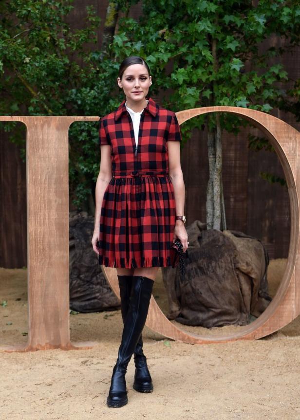 Olivia Palermo trägt ein rot-schwarzes Kleid und schwarze Stiefel vor einem „Dior“-Schriftzug.