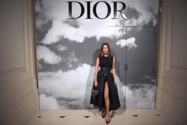 Eine Frau posiert vor einem Dior-Logo und einem Wolkenhintergrund.