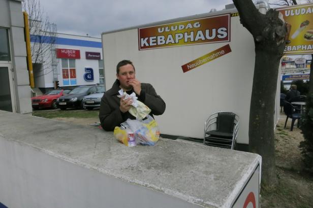 Ein Mann isst vor dem „Uludag Kebaphaus“ mit dem Hinweis „Neuübernahme“.