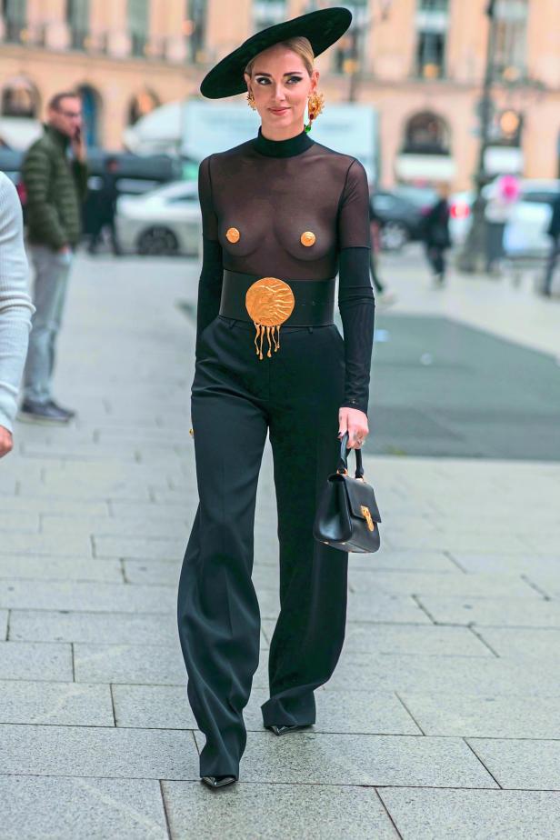 Chiara Ferragni in einem schwarzen, transparenten Oberteil, einer Hose und einem Hut auf einer Straße.