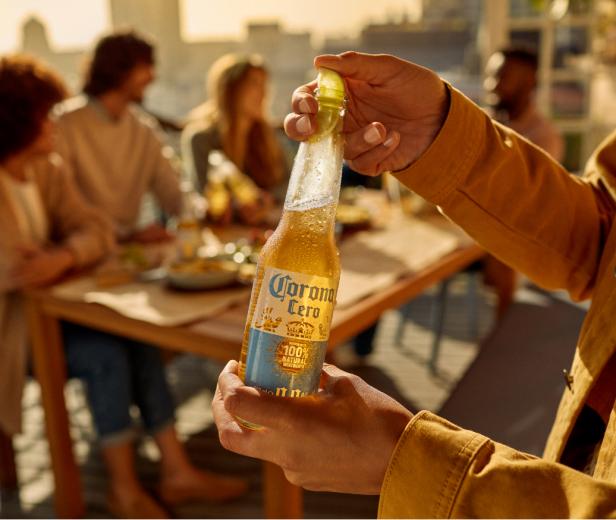 Eine Person hält eine Flasche Corona Cero mit Limette vor einer Gruppe von Menschen.