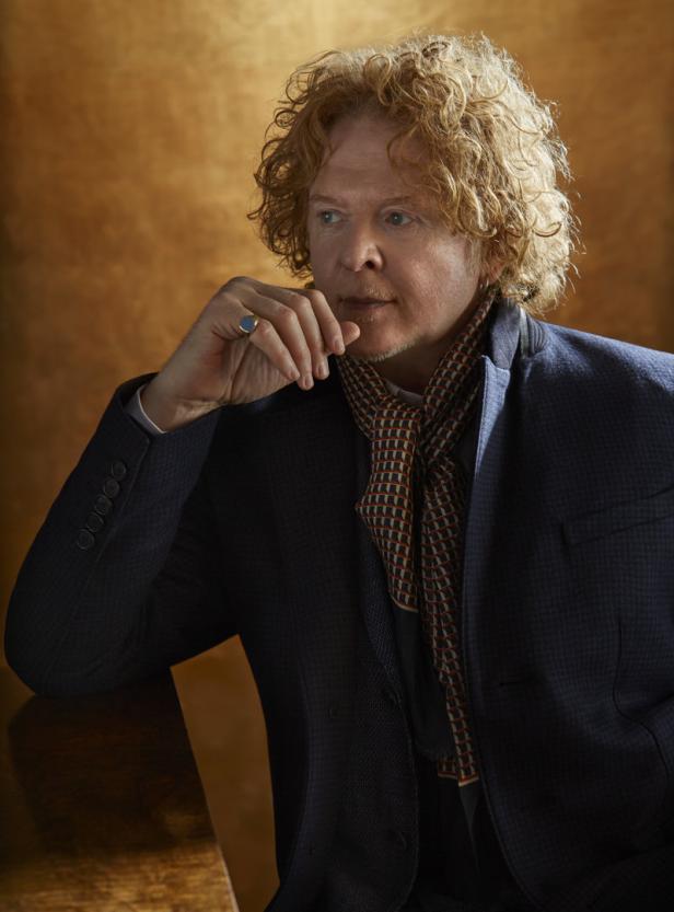Mick Hucknall, der Sänger von Simply Red, posiert in einem dunklen Anzug und einem gemusterten Schal.