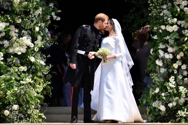 Prinz Harry und Meghan Markle küssen sich nach ihrer Hochzeit vor einem mit Blumen geschmückten Eingang.