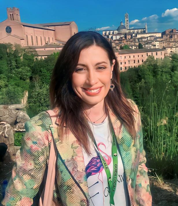 Eine lächelnde Frau vor der Skyline von Siena, Italien.