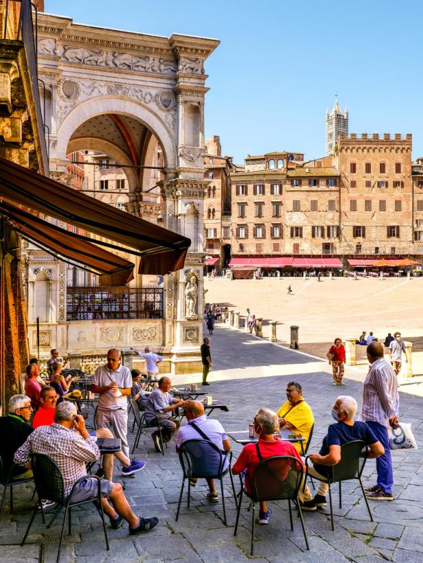 Menschen sitzen in einem Straßencafé auf der Piazza del Campo in Siena.