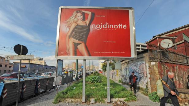 Eine Werbung für „nojdinotte“ Unterwäsche mit Noemi Letizia auf einer Plakatwand am Straßenrand.