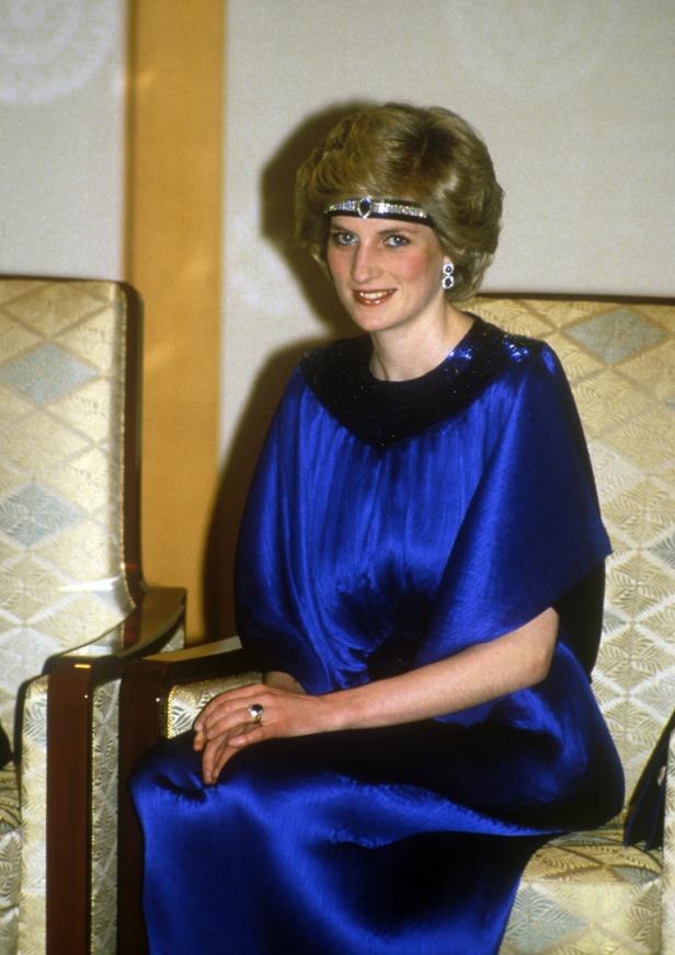 Prinzessin Diana sitzt in einem blauen Kleid und mit einem Diadem auf einem Stuhl.