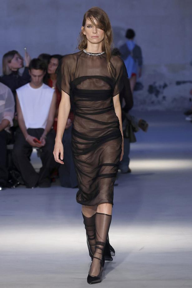 Eine Frau präsentiert ein transparentes, schwarzes Kleid auf einem Laufsteg.