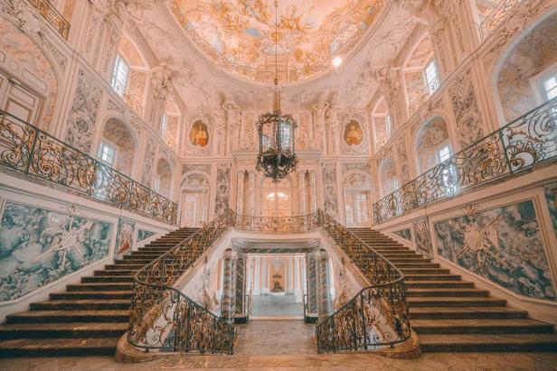 Eine prunkvolle Treppe führt in einem reich verzierten Schloss nach oben.