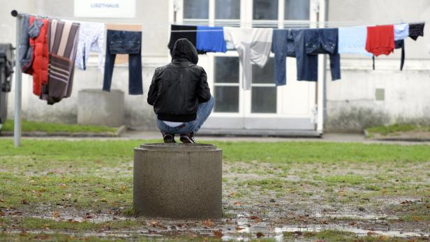 Eine Person hockt auf einem Betonrohr, im Hintergrund hängt Wäsche zum Trocknen.