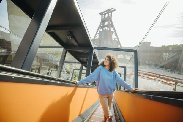 Eine Frau fährt auf einer Rolltreppe mit Blick auf ein Industriegebäude.