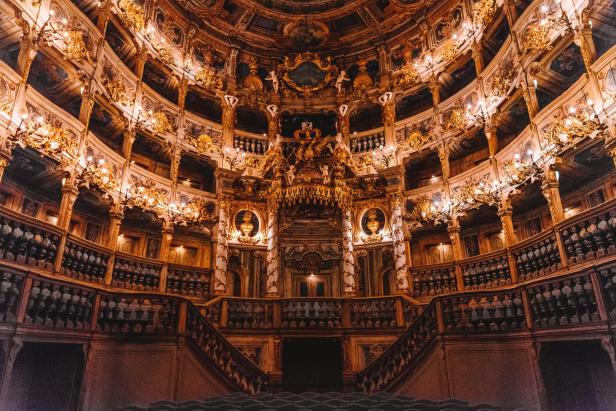Innenansicht eines prunkvollen Theaters mit goldenen Verzierungen und mehreren Rängen.