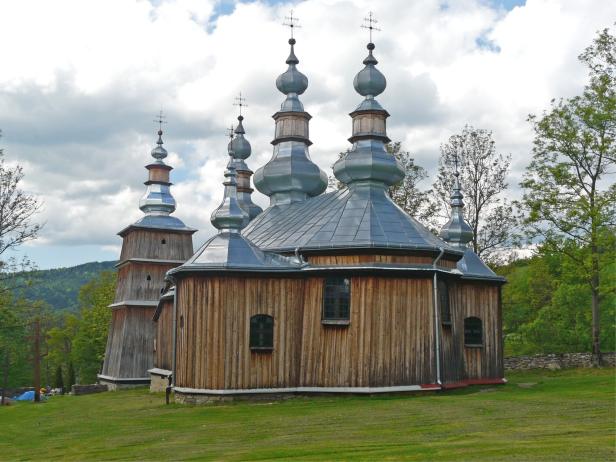 Eine hölzerne orthodoxe Kirche mit mehreren Kuppeln und einem Turm steht auf einer grünen Wiese.