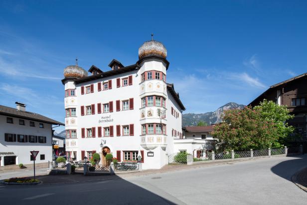 Der Gasthof Herrenhaus in Tirol mit traditioneller Architektur vor blauem Himmel.