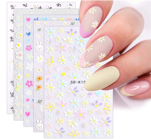 Mehrere Bögen mit Nagelstickern und eine Hand mit beklebten Nägeln.