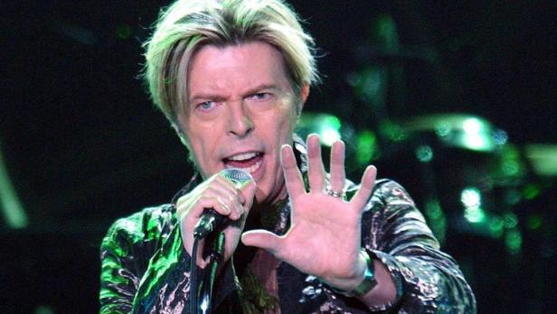 David Bowie singt mit erhobener Hand in ein Mikrofon.