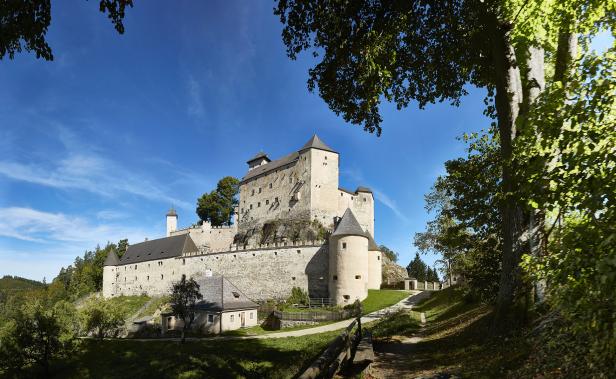 Burg Lockenhaus thront auf einem Felsen unter blauem Himmel.