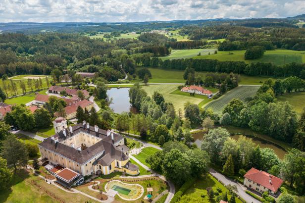 Luftaufnahme eines Schlosses mit gelber Fassade und weitläufigem Parkgelände.
