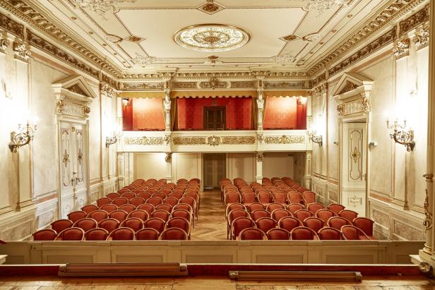 Blick auf den Zuschauerraum eines Theaters mit roten Sitzen und reich verzierter Decke.