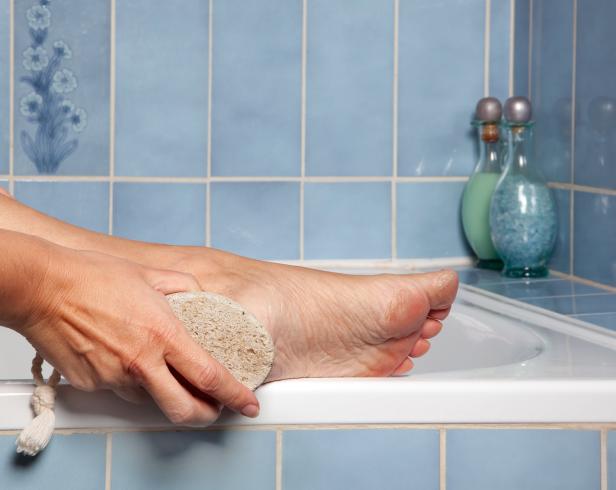 Eine Frau benutzt einen Bimsstein, um ihre Füße im Badezimmer zu peelen.