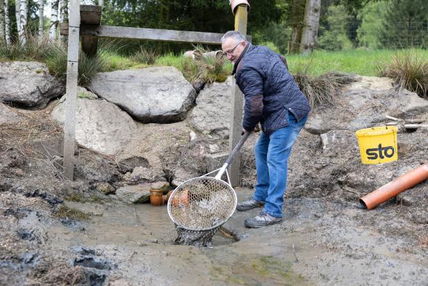 Ein Mann fischt mit einem Kescher in einem schlammigen Graben.
