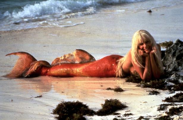 Eine Frau, als Meerjungfrau verkleidet, liegt am Strand.
