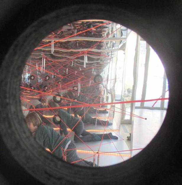 Kinder kriechen unter roten Laserstrahlen in einem Spiegellabyrinth hindurch.